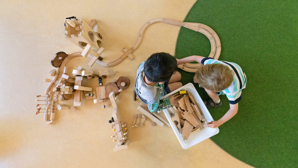 Kinder der GA Sport-Kita spielen zusammen mit einer Eisenbahn aus Holz.