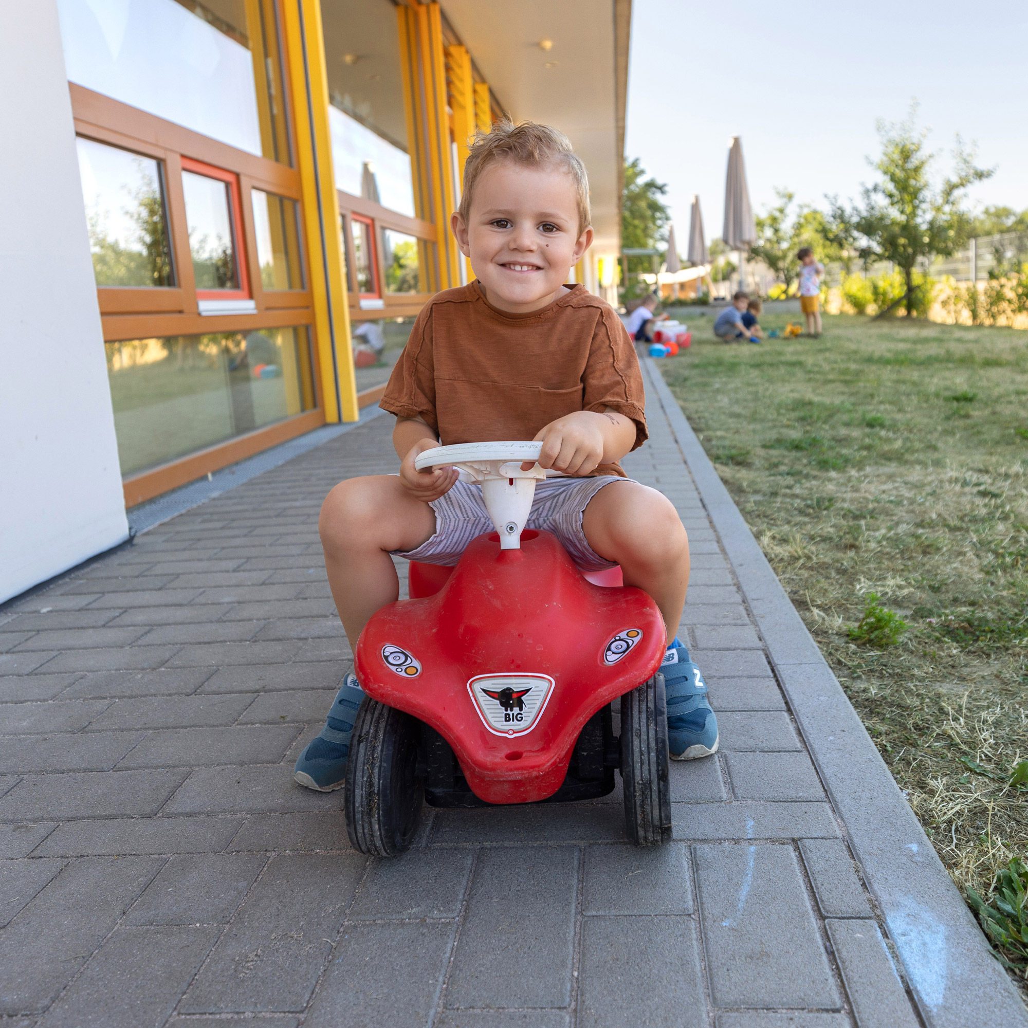 Ein Kind der SGA Sport-Kita fährt im Garten Bobby-Car.